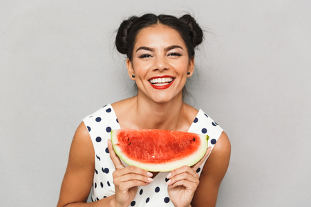Portrait of a satisfied young woman in summer dress isolated, holding watermelon sliceの写真素材