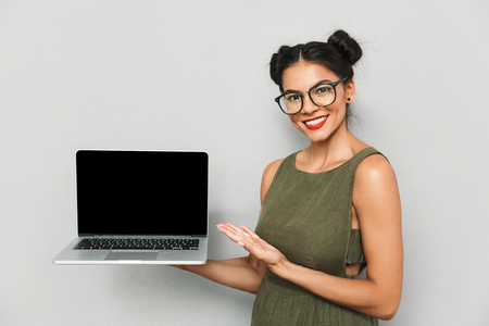 Portrait of a happy young woman isolated, showing blank screen laptop computerの写真素材