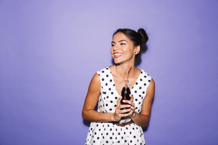 Portrait of a happy young woman in summer dress isolated, holding bottle with fizzy drink, looking at copy spaceの写真素材