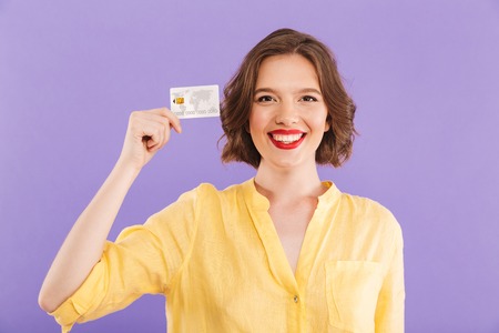 Portrait of a smiling young woman showing plastic credit card isolated over violet backgroundの写真素材