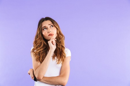 Portrait of a pensive young girl standing isolated over violet background, looking at copy space