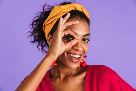 Close up portrait of a smiling young african woman in headband over violet background, showing ok gestureの写真素材