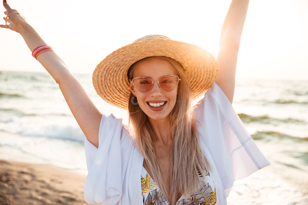 Close up of a pretty young girl in summer hat and sunglasses at the beach looking at camera, having funの写真素材