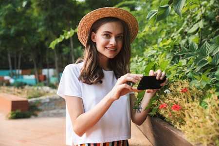 Smiling young girl making photos with camera at the park outdoors in summer