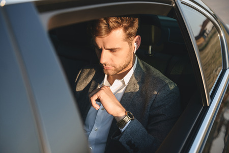 Portrait of concentrated caucasian man wearing businesslike suit and earpod back sitting while...