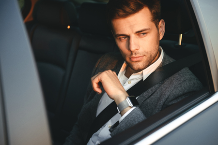 Portrait of serious businessman wearing classic suit back sitting while riding in car with safety beltの写真素材