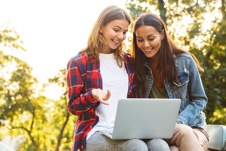 Picture of young amazing women friends students sitting in the park using laptop computer.の写真素材