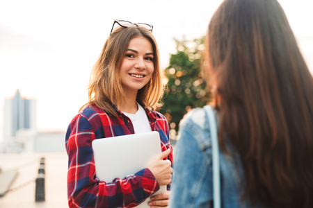 Image of happy young beautiful ladies students walking in the park talking with each other.の写真素材