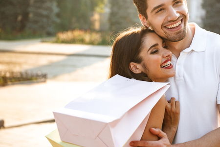 Photo of young cute loving couple walking outdoors while holding shopping bags.の写真素材