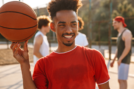Photo of multiethnic men playing basketball at the playground outdoor and american guy spinning ball on his fingerの写真素材