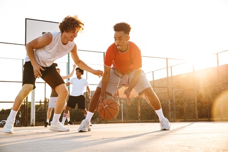 Group of young cheerful multiethnic men basketball players playing basketball at the sport ground
