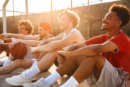 Group of young laughing multiethnic men basketball players resting at the sport ground, talkingの写真素材