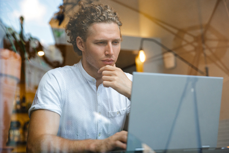 Serious curly business man using laptop computer while sitting by the table in cafeの写真素材