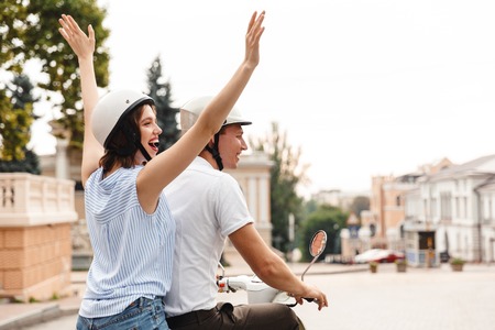 Back view of happy young couple in crash helmets riding on scooter together outdoorsの写真素材