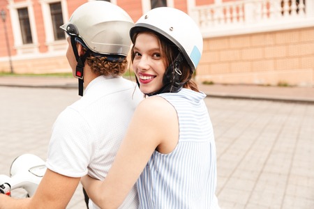 Portrait of a smiling young couple in helmets riding on a motorbike together at the city streetの写真素材
