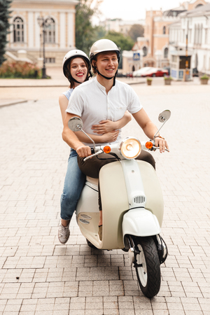 Portrait of a happy young couple in helmets riding on a motorbike together at the city streetの写真素材