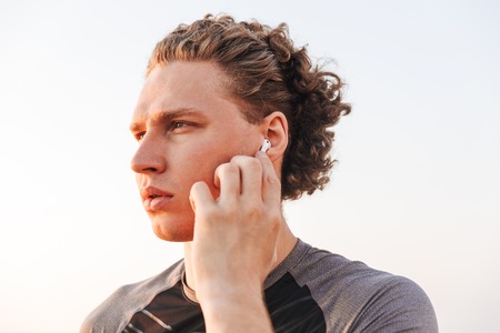 Photo of young handsome sports man outdoors on the beach listening music with earphones.の写真素材