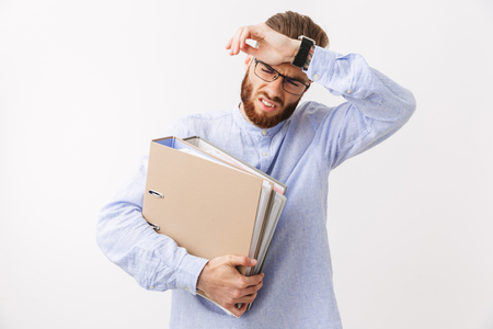 Portrait of an exhausted young bearded man standing isolated over white, holding foldersの写真素材