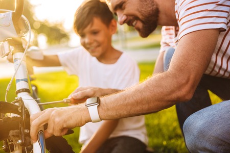 Cropped image of smiling father and his son having fun together at the green park, fixing bicycle togetherの写真素材