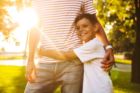 Happy little boy hugging his dad while standing at the parkの写真素材