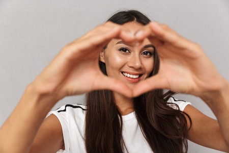 Photo of excited cheerful young woman isolated over grey background showing heart love gesture.の写真素材
