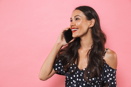 Photo of excited happy young woman isolated over pink background talking by mobile phone.の写真素材