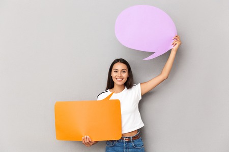Image of young happy emotional woman posing isolated over grey background holding speech bubble.の写真素材