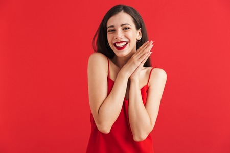Portrait of a lovely young woman in dress isolated over red background, holding hands at her faceの写真素材