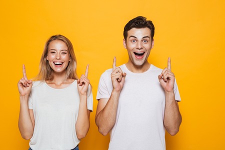 Photo of happy excited young loving couple standing isolated over yellow wall background pointing.の写真素材