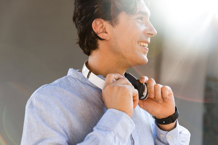 Smiling young casual man with headphones standing at the city streetの写真素材