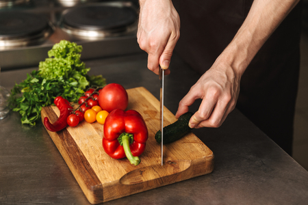 Close up of a man chef hands chopping vegetables on a cutting board at he kitchenの写真素材