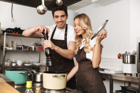 Image of happy young friends loving couple chefs on the kitchen cooking.の写真素材