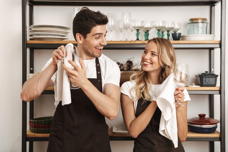 Image of happy excited young friends loving couple chefs on the kitchen wipe glasses.の写真素材