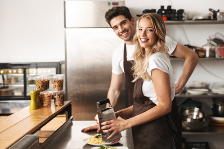 Image of happy young friends loving couple chefs on the kitchen cooking.