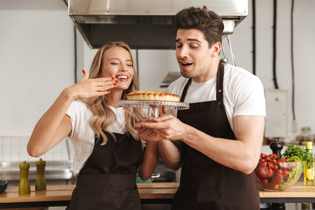 Image of happy young friends loving couple chefs standing on the kitchen holding smelling cake.の写真素材