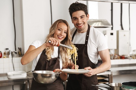 Image of happy young friends loving couple chefs on the kitchen cooking.の写真素材