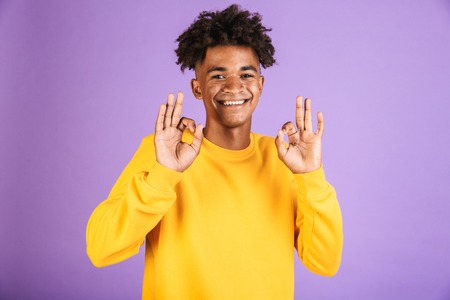 Portrait of a smiling young afro american man dressed in sweatshirt showing ok isolated