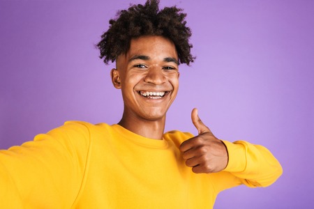 Portrait of a cheerful young afro american man dressed in sweatshirt taking a selfie isolated, showing thumbs upの写真素材