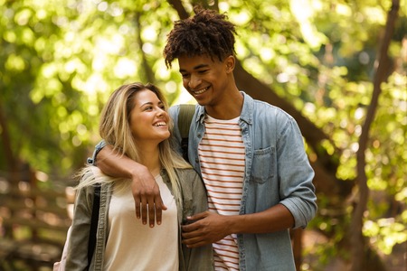 Cheerful young multiethnic couple spending time together at the park, walking, huggingの写真素材