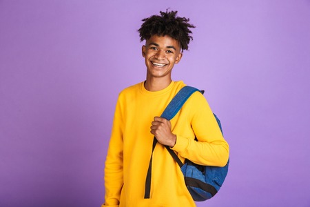 Portrait of a cheerful young afro american man dressed in sweatshirt carrying backpack isolatedの写真素材
