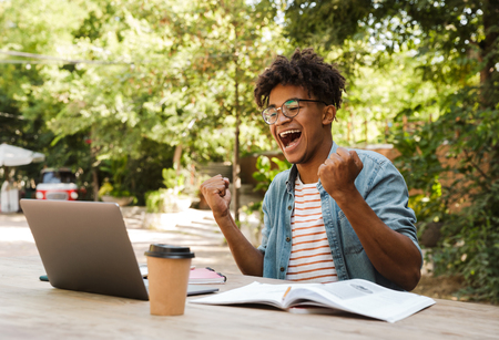 Joyful young african man student studying at the park with laptop computerの写真素材