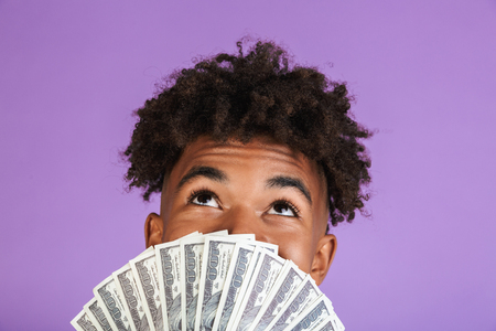 Close up portrait of a happy young afro american man in sweatshirt isolated, showing money banknotes at his faceの写真素材