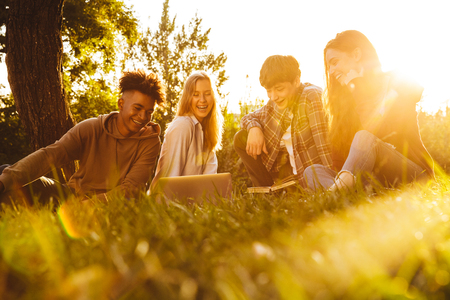 Group of laughing multhiethnic students doing homework together at the park, using laptop computerの写真素材