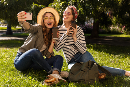 Two excited young girls friends having fun at the park, taking a selfie, having a picnicの写真素材
