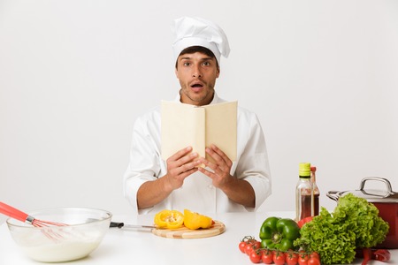 Image of shocked excited young chef man isolated over white wall background cooking reading book.
