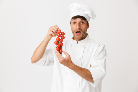 Photo of cheerful excited young chef isolated over white background holding tomatoes.の写真素材