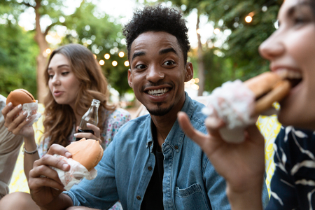 Image of happy young friends party outdoors in park having fun eat burgers.