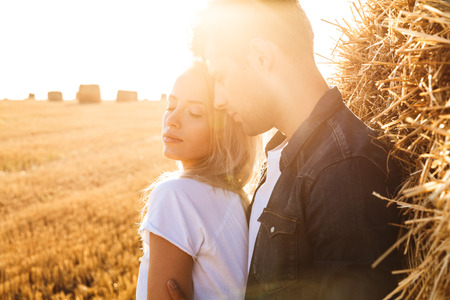 Image of sunlit couple man and woman walking on golden field after harvesting and standing near big...