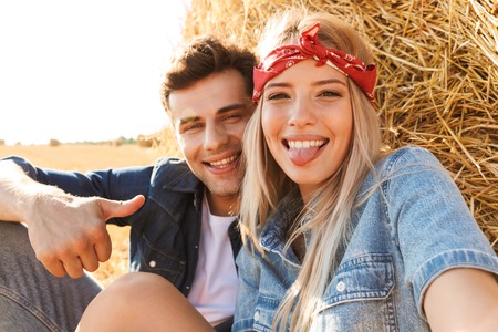 Close up of a cheerful young couple sitting at the wheat field, taking a selfieの写真素材