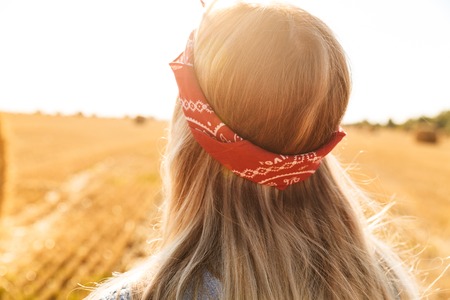 Back view of a young blonde girl in headband at the wheat field looking awayの写真素材